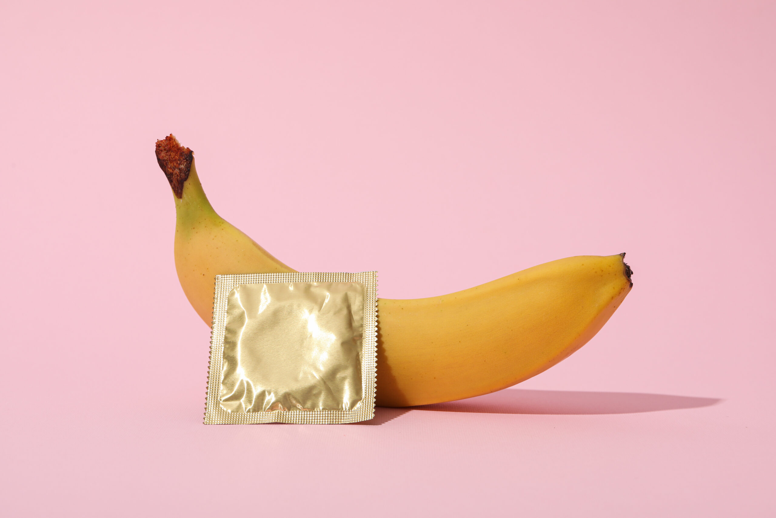 Una banana con un condom su uno sfondo rosa